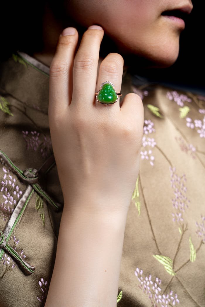 Close-up of a hand wearing a luxurious jade ring against a floral silk background.